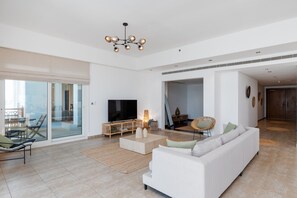 A spacious living room with a large flat-screen TV, a white sofa, and a dining area with a glass wall.