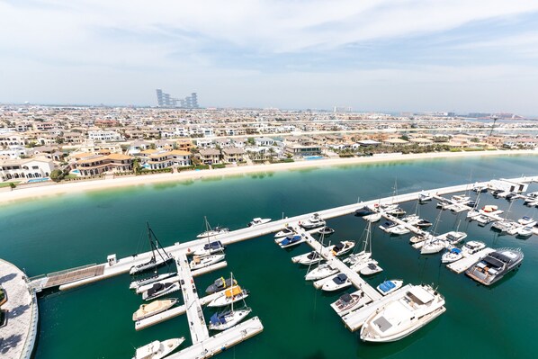 Una marina con varias embarcaciones amarradas, un muelle que se adentra en el agua y un paisaje urbano costero al fondo.