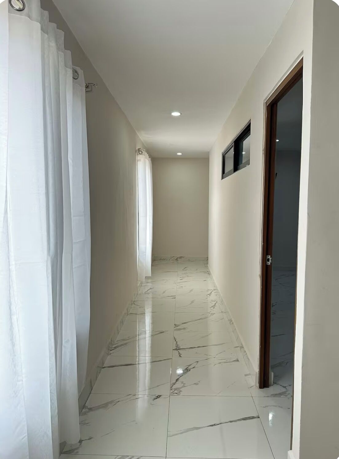 Un couloir doté d’un sol en marbre blanc, de murs blancs et d’une porte en bois.