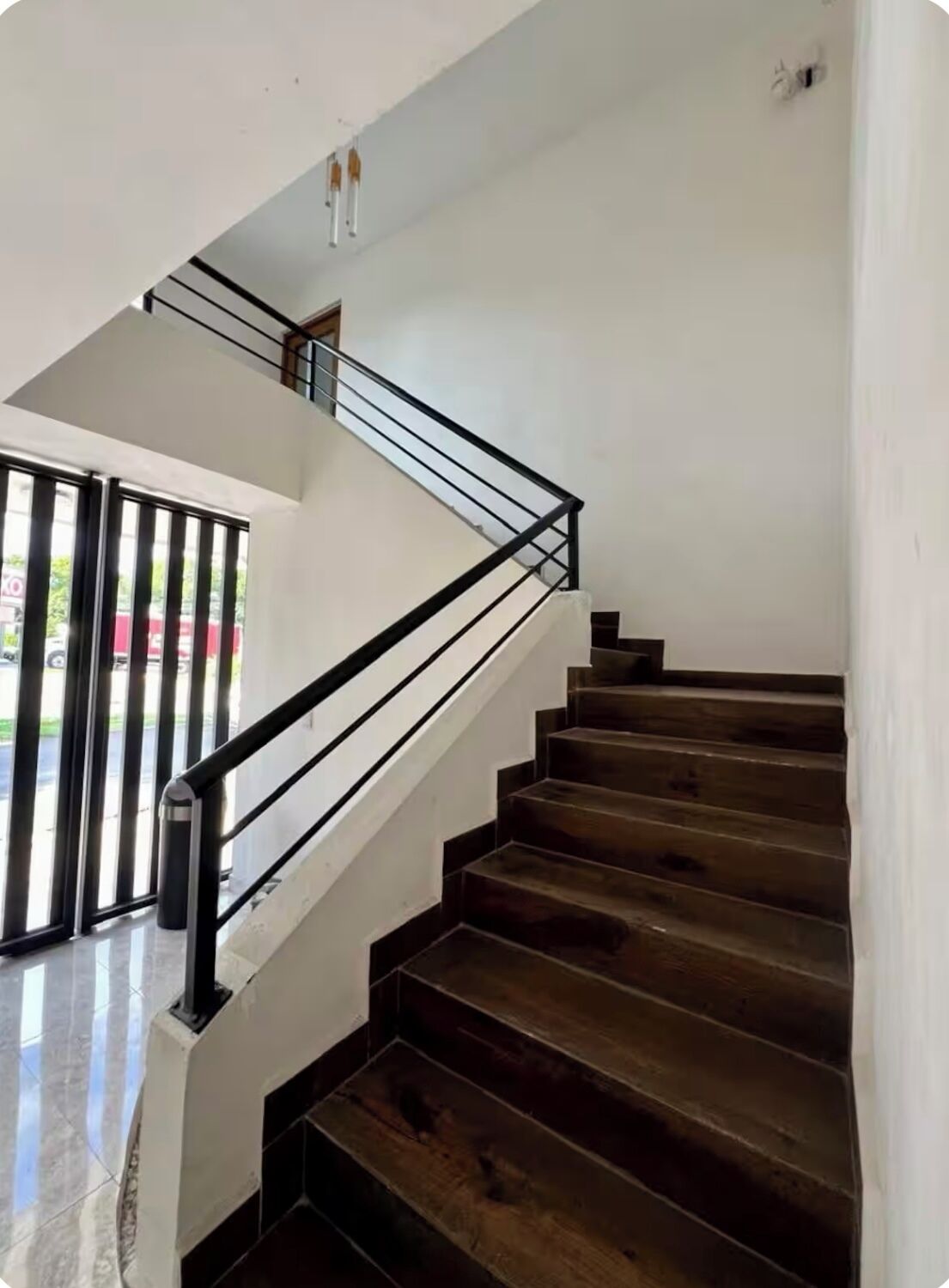 A staircase with dark wooden steps and a black metal railing, leading to a landing with a glass door.