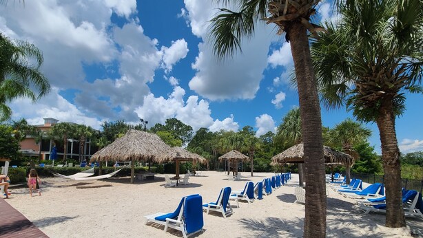 Una playa con sombrillas de paja y sillas de descanso azules.