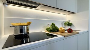 A modern kitchen with a black induction cooktop, a stainless steel pot with spaghetti, fresh vegetables on a wooden board, and a white backsplash. - Salieri Attic (500mt. from St. Mark's Square) (Venecia)