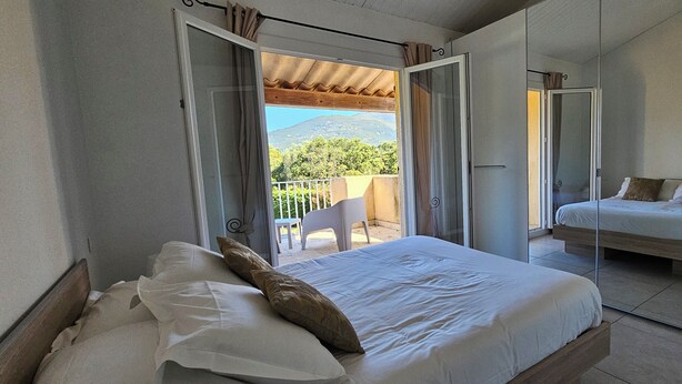 Een slaapkamer met een bed, een balkon met uitzicht op een berg en een los bed in de aangrenzende kamer.