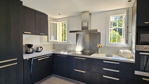 Een moderne keuken met donkere kasten, een roestvrijstalen afzuigkap, een inbouwoven en een raam dat voor natuurlijk licht zorgt.