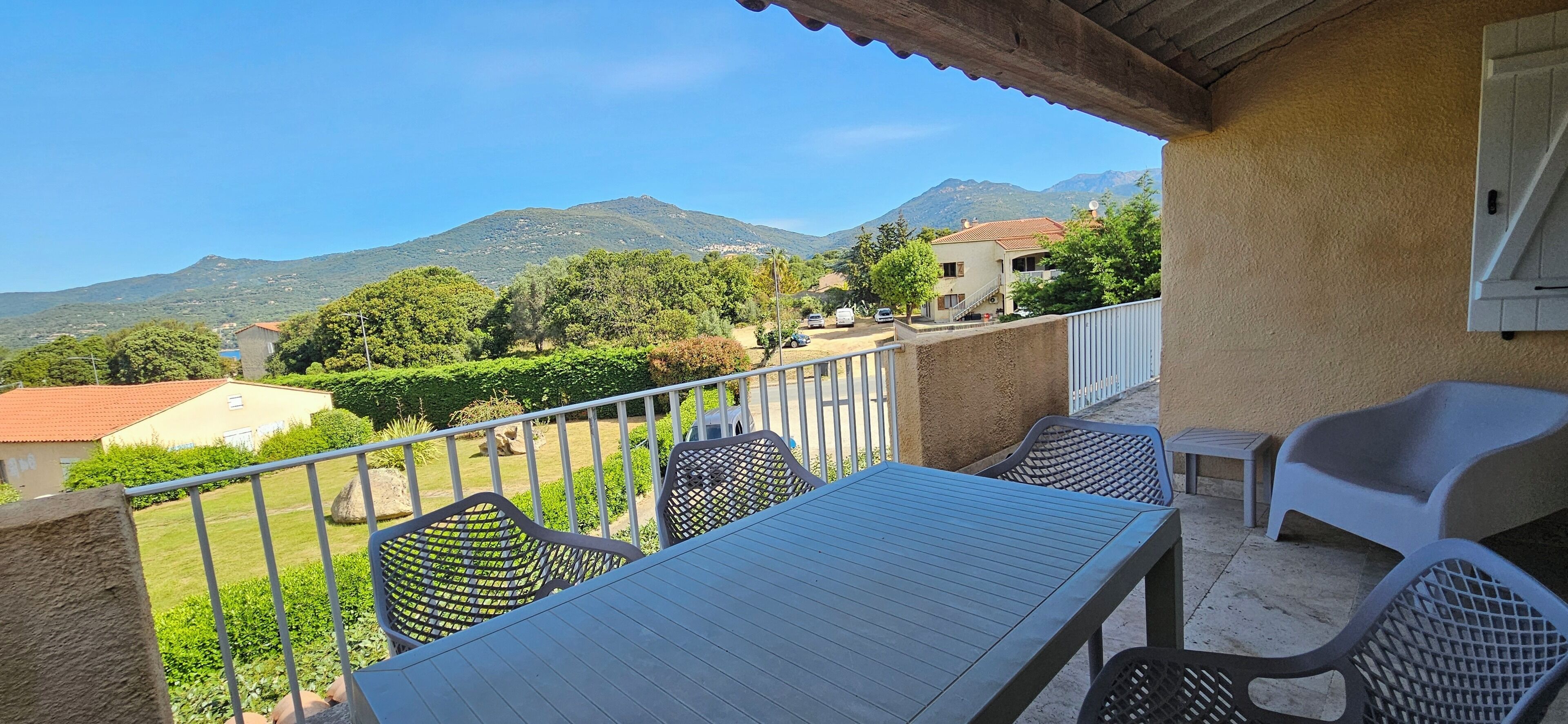 Un balcón con mesa y sillas, con vistas a un paisaje montañoso con casas y vegetación.