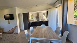 Een moderne woonkamer met een bank, een televisie, een eettafel met stoelen en een keuken op de achtergrond.