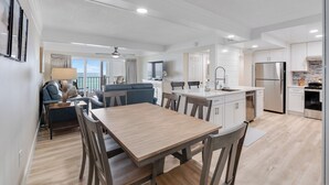 Una cocina moderna con armarios blancos, un refrigerador de acero inoxidable y un comedor con mesa y sillas de madera.