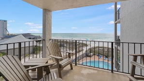 Un balcón con vista a la playa y al océano, sillas de madera y una piscina.