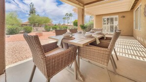 An outdoor patio with a table set for dining, wicker chairs, and a view of the surrounding landscape. - 3BR single-level home in 55+ community (Sun Lakes)