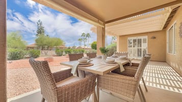 An outdoor patio with a table set for dining, wicker chairs, and a view of the surrounding landscape.