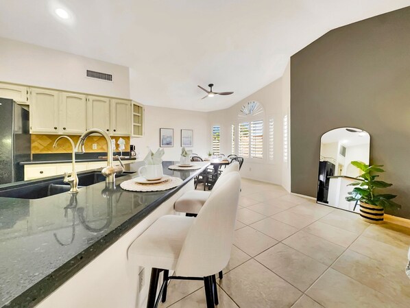 A modern kitchen with a central island, white cabinetry, and a dining area with a white chair and table.