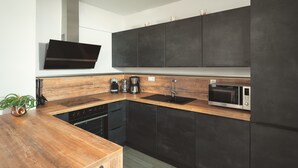 A modern kitchen with dark cabinets, a wooden countertop, a built-in oven, and a coffee maker.