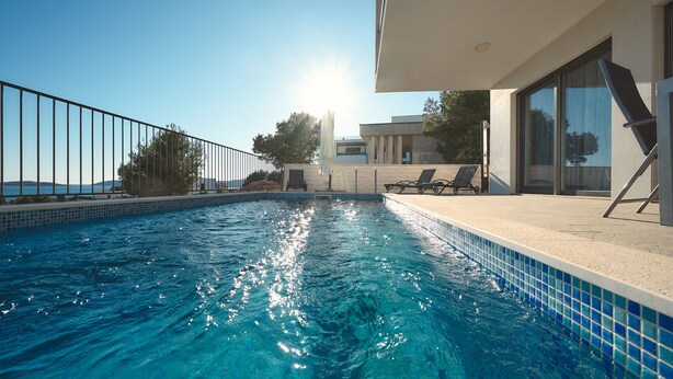 A swimming pool with a clear blue water, surrounded by a metal fence, and a modern building with large windows and a balcony.