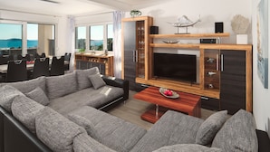 A modern living room with a large grey sectional sofa, a wooden coffee table, and a flat-screen TV mounted on a wooden wall.