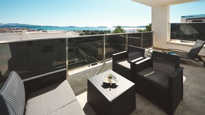 A balcony with outdoor furniture, a glass balustrade, and a view of the city and mountains.