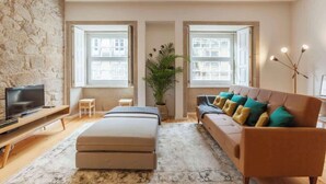 Ein modernes Wohnzimmer mit einer Wand aus Stein, einer Couch mit Kissen, einem Fernseher und einem großen Fenster, das natürliches Licht hereinlässt.
