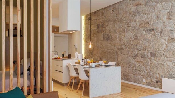 Ein modernes Interieur mit Steinwand, Holzboden, Essbereich mit Stühlen und Tisch sowie eine Couch mit Kissen.