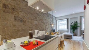 Eine moderne Küche mit Steinwand, einer zentralen Kochinsel und einem Essbereich mit Sofa und Pflanze.