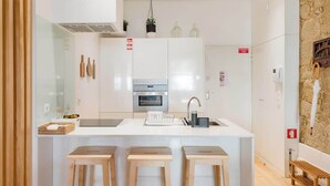Una cocina moderna con una isla central, taburetes de bar, horno empotrado y una pared decorativa de piedra.