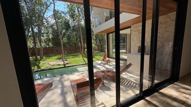 A modern interior with large glass doors leading to an outdoor patio area with a pool and seating. - Beautiful house - Riviera Maya. Mayakoba Country Club (Playa del Carmen)