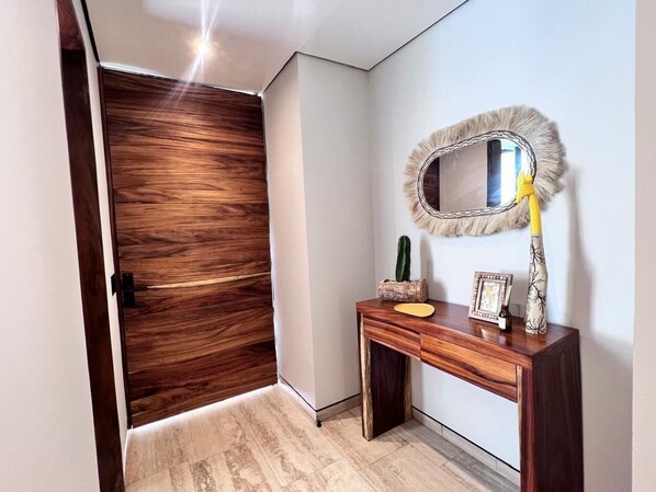 Un couloir avec une porte en bois, une console en bois surmontée d’un miroir et un cactus posé sur la console.