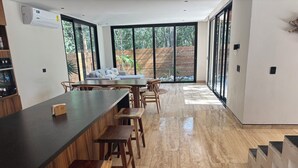 A modern kitchen with a long counter, wooden stools, and large windows offering a view of the outdoors. - Beautiful house - Riviera Maya. Mayakoba Country Club (Playa del Carmen)