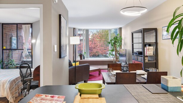 A modern living room with a dining area, large windows, and a bookshelf.