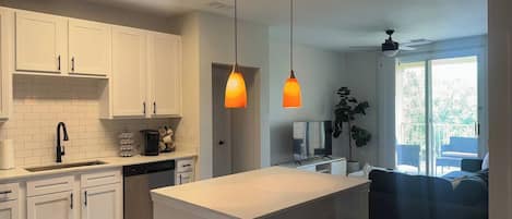 Una cocina moderna con armarios blancos, una isla central con taburetes, lavavajillas integrado y un amplio ventanal con vistas a un balcón.