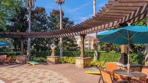 Un patio al aire libre con pérgola, mobiliario y palmeras.