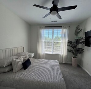 A bedroom with a bed, a ceiling fan, a window with curtains, and a potted plant.
