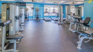 Un gimnasio con diversas máquinas de ejercicio, una banca y un ventilador de techo.