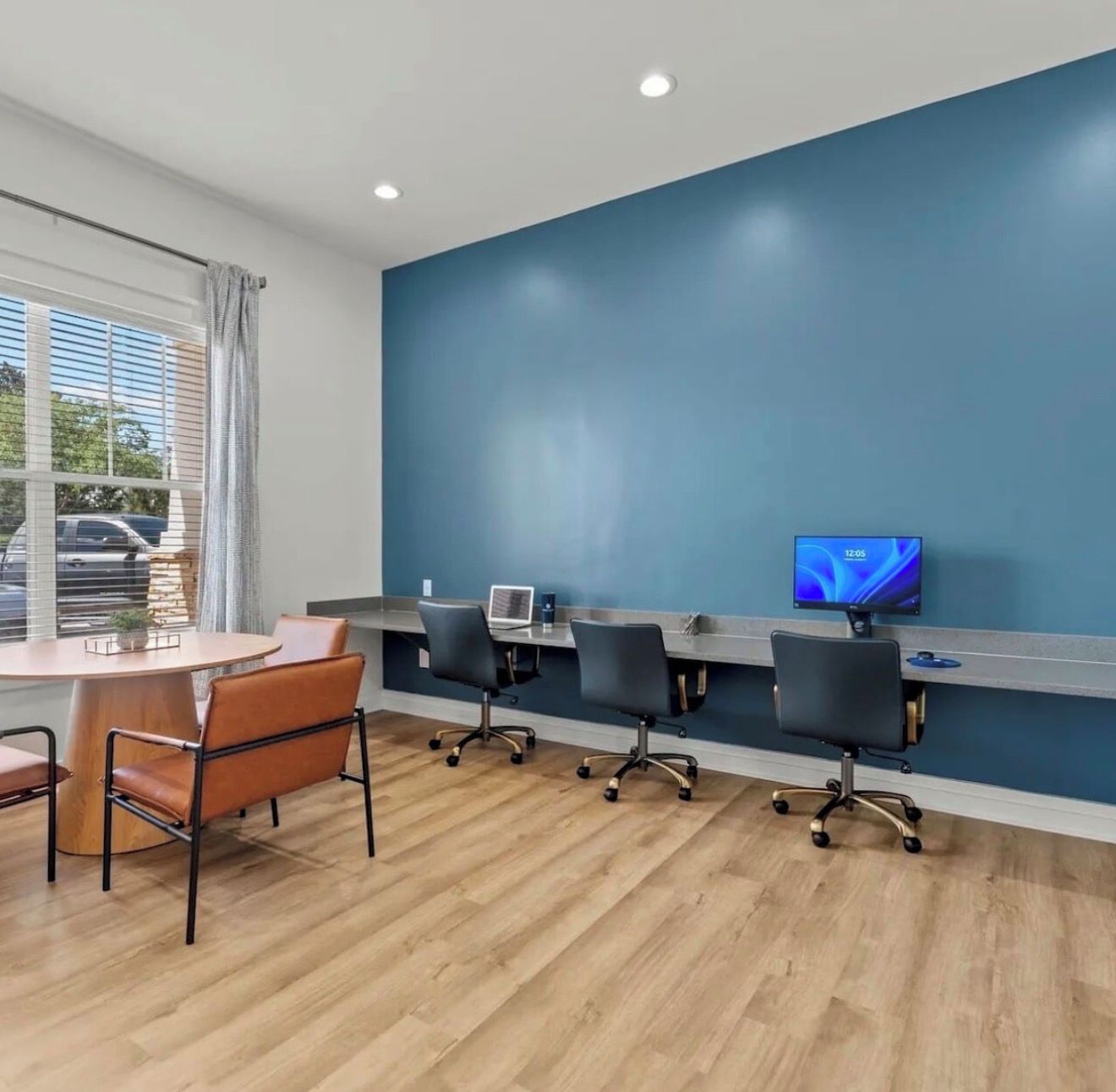 A conference room with a long table, four chairs, a laptop, and a television on the wall.