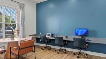 A conference room with a long table, four chairs, a laptop, and a television on the wall.