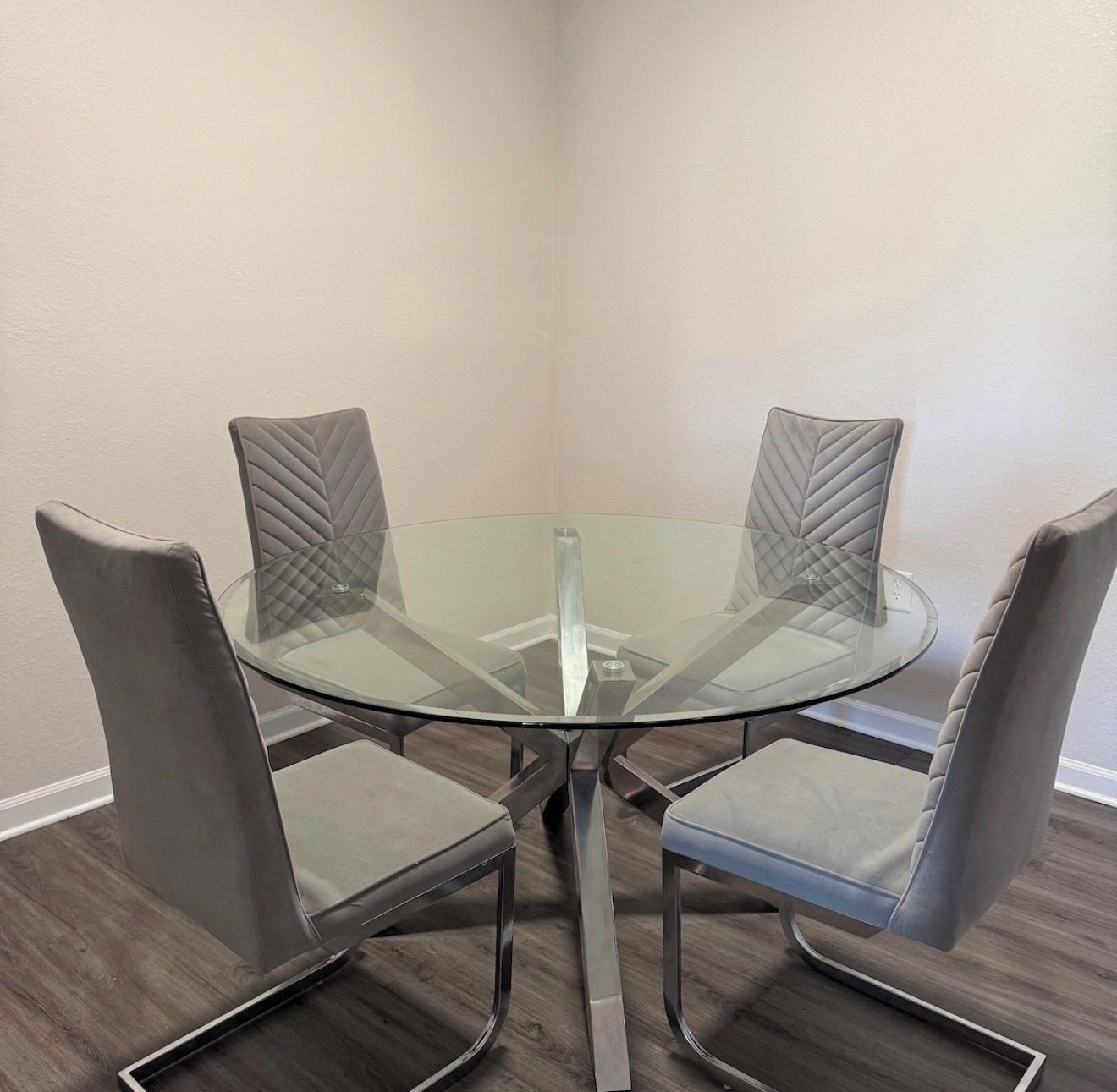 Un coin repas avec une table en verre entourée de quatre chaises rembourrées.