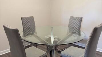 A corner dining area with a glass table surrounded by four cushioned chairs.