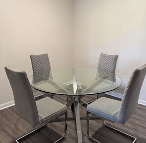A corner dining area with a glass table surrounded by four cushioned chairs. - Heart of Bartram Escape! (Jacksonville)