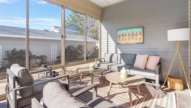 A modern living room with a gray sofa, two wooden coffee tables, and a large window offering a view of neighboring houses. - Chic Escape  w/ Courtyard, Game Lounge, Hot Tub! (Douglas)