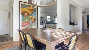 A dining area with a wooden table and chairs, a hanging light fixture, and a kitchen in the background. - Chic Escape  w/ Courtyard, Game Lounge, Hot Tub! (Douglas)