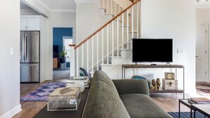 A living room with a staircase, a flat-screen TV, and a sofa. - Chic Escape  w/ Courtyard, Game Lounge, Hot Tub! (Douglas)