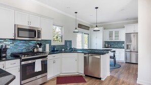 A modern kitchen with white cabinets, stainless steel appliances, and a blue backsplash. - Chic Escape  w/ Courtyard, Game Lounge, Hot Tub! (Douglas)