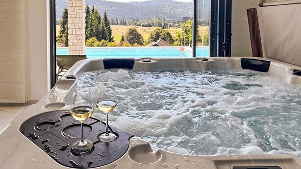 Ein Whirlpool mit zwei Weingläsern und einer Fernbedienung, mit Blick auf einen Pool und eine schöne Landschaft.