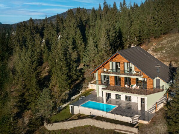 Une maison moderne dotée d’un grand balcon, d’une piscine et donnant sur une colline boisée.