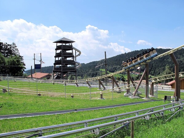 Eine Achterbahn mit einem hohen Turm im Hintergrund, umgeben von grünen Feldern und Bäumen.