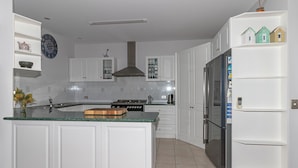 Une cuisine moderne avec des meubles blancs, un îlot central, une cuisinière et un réfrigérateur.