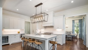 A spacious kitchen with white cabinetry, a large island with stools, and a hanging light fixture.