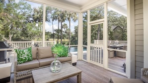 A covered outdoor deck with a sofa, a table, and a grill.