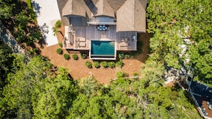 An aerial view of a large house with a swimming pool, surrounded by dense greenery.
