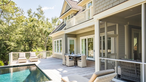 A two-story house with a large deck, a swimming pool, and outdoor furniture.