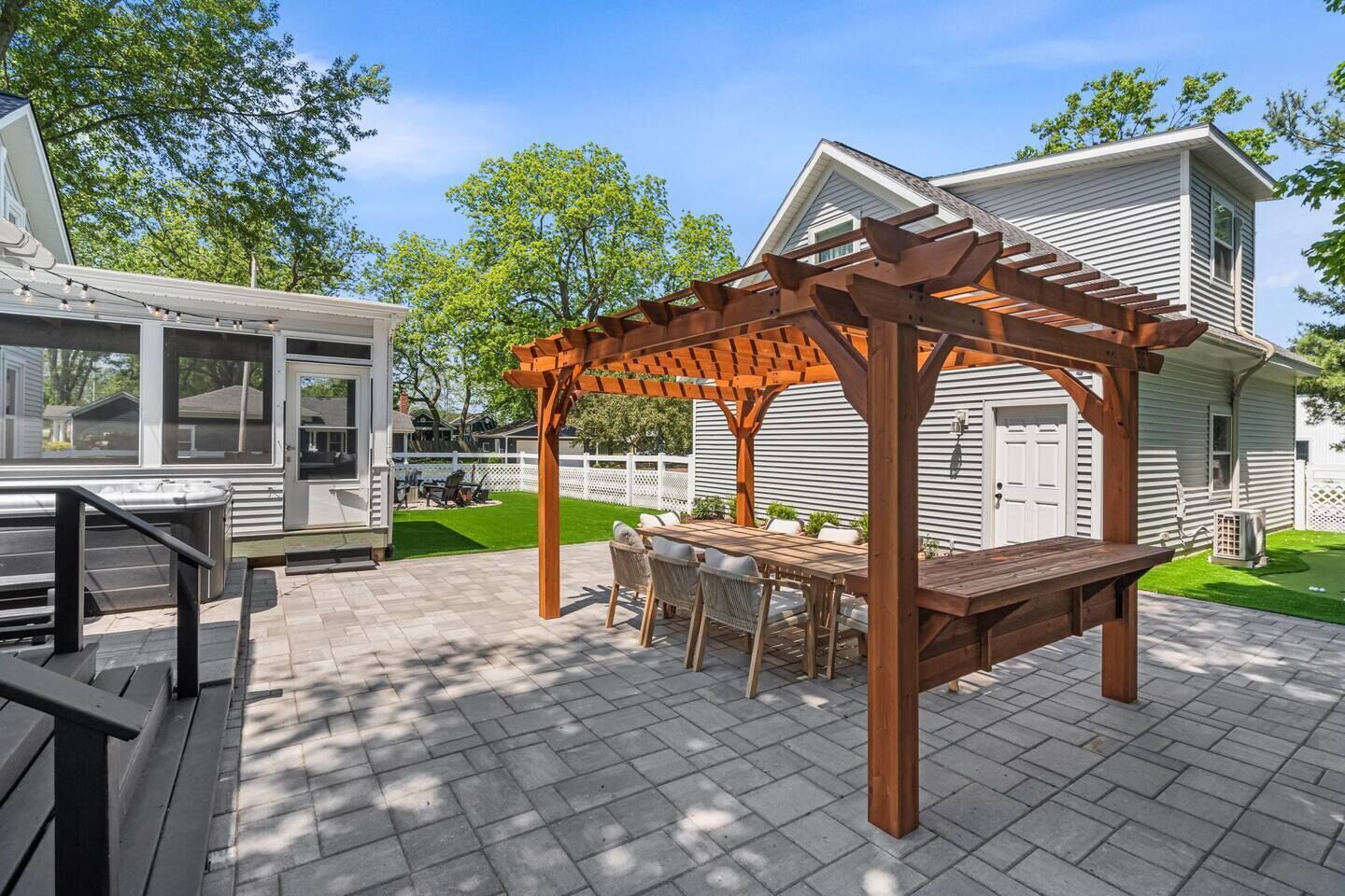 A covered patio with a wooden pergola, outdoor seating, and a view of a house.