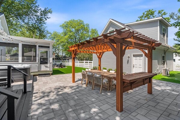 A covered patio with a wooden pergola, outdoor seating, and a view of a house.